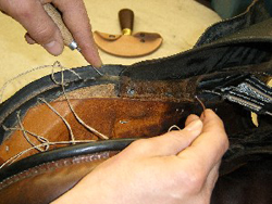 Zaakvoerder Jean-Paul van Paardenwinkel Hopa Sport naait de achterkant van de kussens van een zadel opnieuw in met een daarvoor gebogen naald