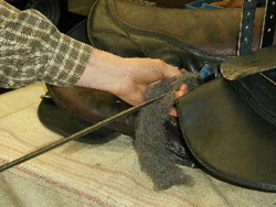 Zaakvoerder Jean-Paul van Paardenwinkel Hopa Sport past de kussenvulling van een zadel aan met wol in functie van een specifieke paardenrug